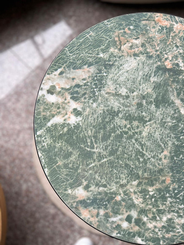 Round marble table with green and pink veining on a blurred background
